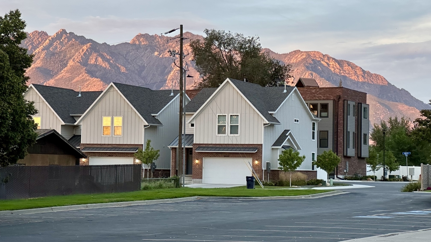 A suburban street is lined with modern houses, set against a backdrop of mountains illuminated by the setting sun.